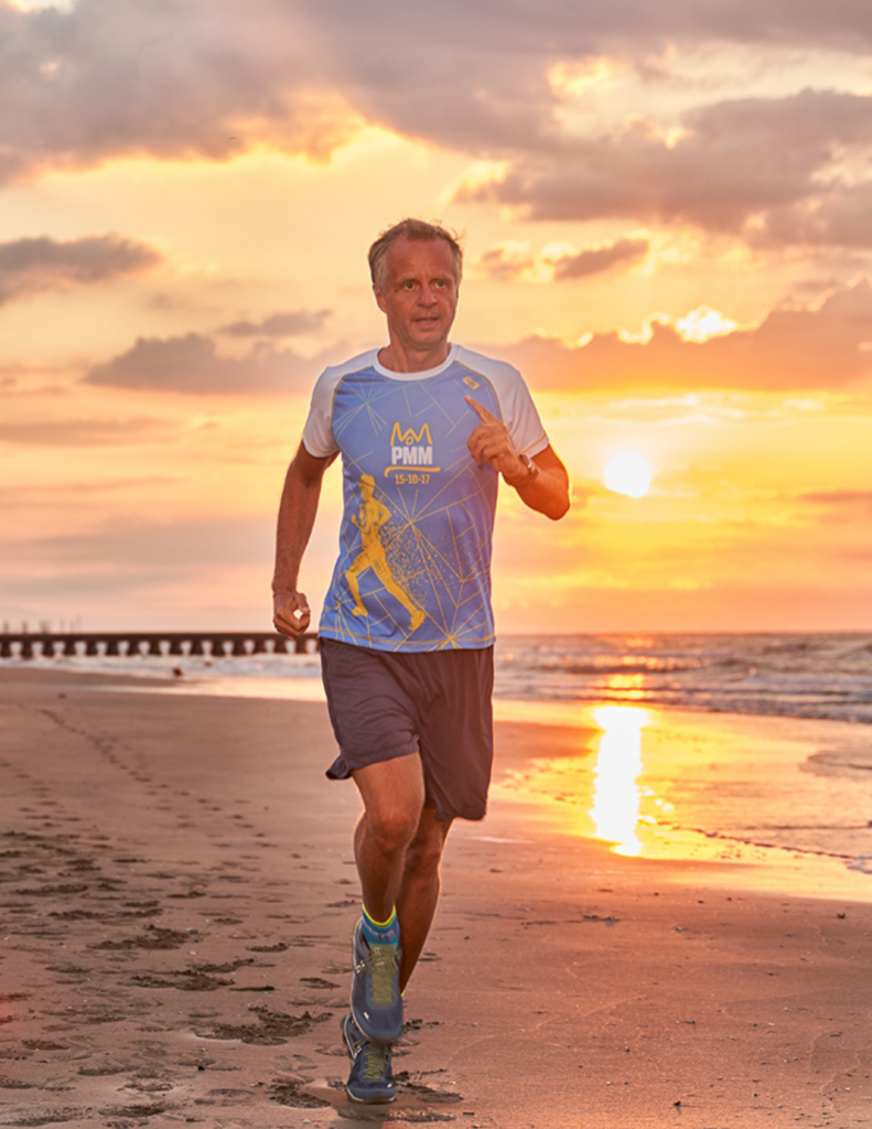 Univ.-Prof. Dr. Johannes Drach joggt am Strand bei Sonnenuntergang und spricht in die Kamera – Facharzt für Innere Medizin und Lauftrainer beim VO2max Webinar